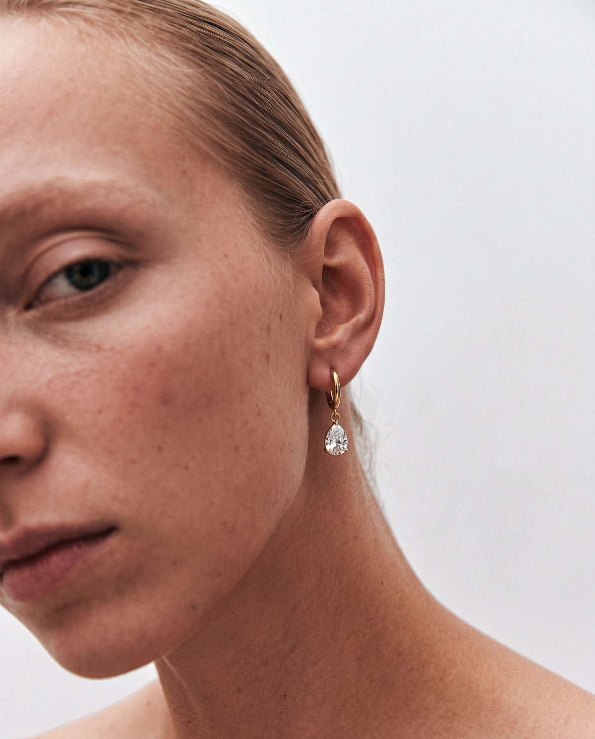 Weekendplans clean jewellery campaign: close-up of a model’s skin and ear wearing a gold hoop with a teardrop crystal.
