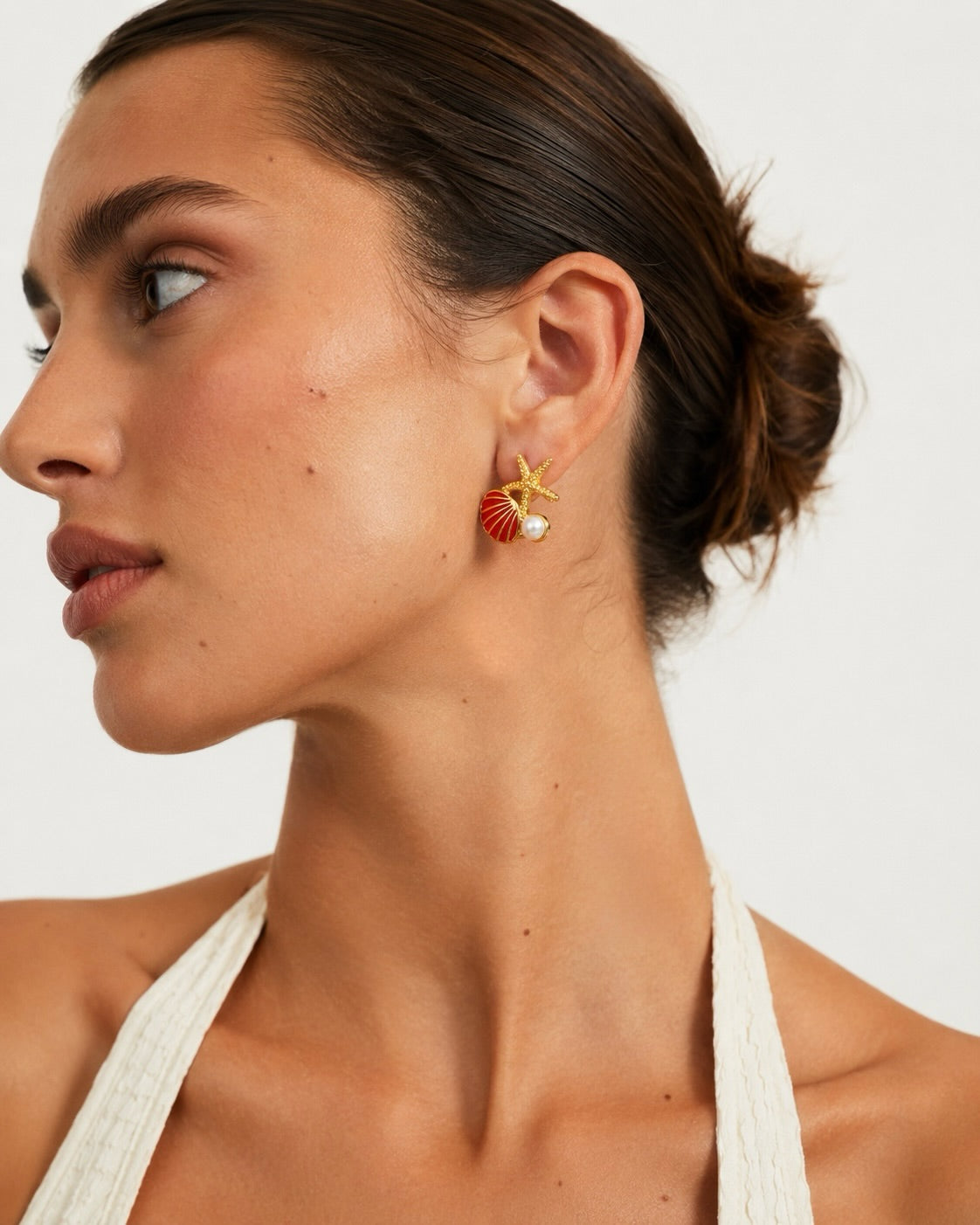 Model wearing Capri Club gold earrings with red shell, starfish and pearl detail